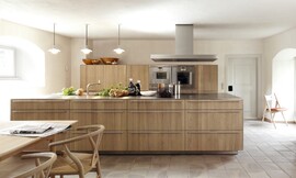 Groot kookeiland met dunne fronten (met brede stanggrepen) en aanrechtblad. Het eiland staat op een sokkel. Achteraan ziet u de hoogkast met apparatuur. Zuordnung: Stil Design-keukens, Planungsart Keuken met keukeneiland