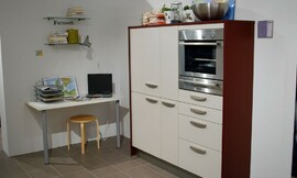 Voorbeeld van een werkplek in de hoek van de keuken. Een simpel tafelblad aan de muur met twee tafelpoten. Keukenkast met gebroken witte fronten en wangen van donker hout. Ingebouwde magnetron-oven-combinatie. Zuordnung: Stil Klassieke keukens, Planungsart U-vormige keuken