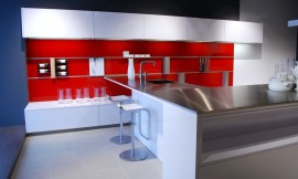 Interessante combinatie van witte fronten en meubels, roestvrij stalen keukenblad en rode achterwand. Hier ziet u de keuken vanaf de kant van de eetbar. Subtiele witte greeploze bovenkasten maken dit hippe keukenconcept af. Zuordnung: Stil Design-keukens, Planungsart keukenblok