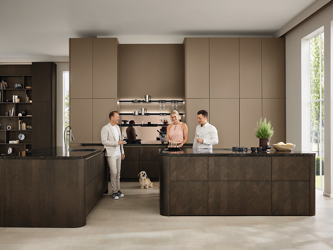Ballerina vertaalt de geometrische vormentaal van de jaren zestig naar een moderne, open woonkeuken. Het intarsia-front in donker gebeitst eikenhout zorgt voor natuurlijke diepte in de ruimte. Twee open kookeilanden zorgen voor een puristisch accent. Zuordnung: Stil Moderne keukens, Planungsart Keuken met keukeneiland
