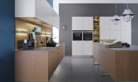 Deze keuken die uit drie elementen bestaat biedt een  combinatie van bijzonder natuurlijk werkende kopereiken fronten met matte sahara-lak oppervlakken. Het eerste keukenblok bevat het fornuis en de spoelbak. De kopereiken onderkasten zijn zwevend aangebracht. Daarboven hangen de bovenkasten in een witte kleur. In de hangkast is een efficiëntie afzuigkap geïntegreerd die geen luchtafvoer behoeft. Perfecte plaats om te werken in de keuken biedt het keukeneiland. Dit eiland is ook van kopereiken en staat op drie open metalen poten. Het andere wandblok, in dezelfde lichte kleur als de hangkasten, is hoog en biedt behalve veel bergruimte ook de nodige apparatuur. Midden in het hoge keukenblok bevindt zich een open kast, waar weer de kopereiken tint in terugkomt. Al met al een moderne keuken met een harmonische en rustige uitstraling met voldoende berg- en werkruimte. Zuordnung: Stil Landelijke keukens, Planungsart Keuken met keukeneiland