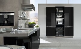 Design eilandkeuken met zwarte hoogglans fronten en metallic tinten. Het aanrechtblad van het keukeneiland loopt direct over in een bartafel. Design afzuigkap met afgeronde hoeken en zwart. Op deze detailfoto ziet u de subtiel afgeronde grepen aan de fronten en de afzuigkap. Zuordnung: Stil Design-keukens, Planungsart keukenblok