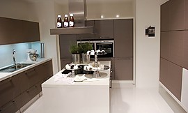 U-vormige keuken met kookeiland in het midden. Mat grijze fronten en witte aanrechtbladen. De inductie-kookplaten bevinden zich op het kookeiland voor een praktische workflow. Zuordnung: Stil Design-keukens, Planungsart U-vormige keuken