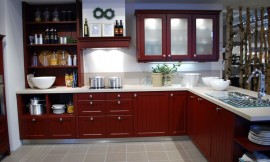 Landelijke keuken met cassette fronten (knopgrepen) in de bijzondere kleur indisch rood. Het aanrechtblad in lichtere tint contrasteert met de rest van de keuken. Bovenkasten met matglazen deurtjes. Links is open opbergruimte te vinden. De afzuigkap is ingebouwd in een schouw. Zuordnung: Stil Landelijke keukens, Planungsart Keuken met keukeneiland