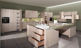 Moderne behaaglijkheid en absolute elegantie. Het oppervlakte is gebeitst in de tint "zilver eik", waardoor deze topkeuken herinnert aan de natuurlijkheid van oude versleten houtplanken. Het binnenwerk van de lades in massief notenhout biedt een aangenaam, warm contrast met de koelere tint van de buitenkant van de meubels. Zuordnung: Stil Moderne keukens, Planungsart Keuken met keukeneiland