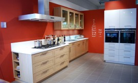 Moderne keuken met eiken houten cassette fronten. Het fornuisgedeelte komt circa 20 cm naar voren ten opzichte van de rest van het aanrecht. Het witte aanrechtblad is verbonden met een eveneens wit achterwandje van 15 cm. Bovenkasten met glazen deurtjes. Zuordnung: Stil Moderne keukens, Planungsart Open keuken (woonkeuken)