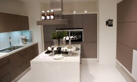 U-vormige keuken met kookeiland in het midden. Mat grijze fronten en witte aanrechtbladen. De inductie-kookplaten bevinden zich op het kookeiland voor een praktische workflow. Zuordnung: Stil Design-keukens, Planungsart Keuken met keukeneiland