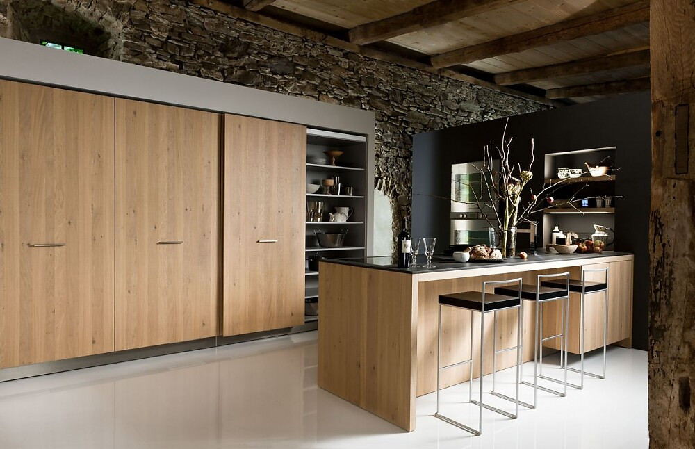 U-vormige keuken met keukeneiland en zitgelegenheid. Optisch wordt de keuken gedragen door het ruwe eiken fineer met verticale tekening. Een robuust oppervlakte contrasteert mooi met de koele rvs-apparatuur. Het keukeneiland is van een dun zwart glanzend aanrechtblad voorzien. Zuordnung: Stil Moderne keukens, Planungsart Keuken met keukeneiland