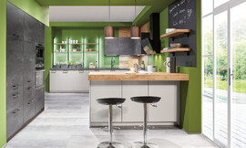 Dit keukenconcept biedt zich voor het open wonen aan. De hoge kasten dringen zich, geintegreerd in de muur, optisch in de achtergrond.  In het middelpunt staat een keukeneiland met een bar en zitmogelijheid. Zuordnung: Stil Moderne keukens, Planungsart Keuken met keukeneiland