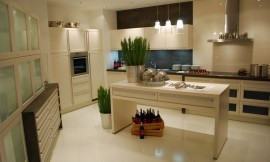 Deze keuken laat u zien wat u met een relatief grote ruimte kunt doen. Verschillende keukenmeubels tegen de wanden en een keukeneiland in het midden. Crèmetinten domineren deze keuken. Het aanrechtblad heeft een donkerdere tint. De fronten hebben brede grepen voor een iets traditionelere look. De kast links heeft glazen deurtjes. Zuordnung: Stil Moderne keukens, Planungsart Open keuken (woonkeuken)