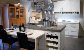 Moderne keuken met kookeiland en open rek voor kookgerei daarboven. Het kookeiland heeft een zithoek met stoelen op normale hoogte aangevoegd en een ingebouwd wijnrek. Zuordnung: Stil Moderne keukens, Planungsart keukenblok