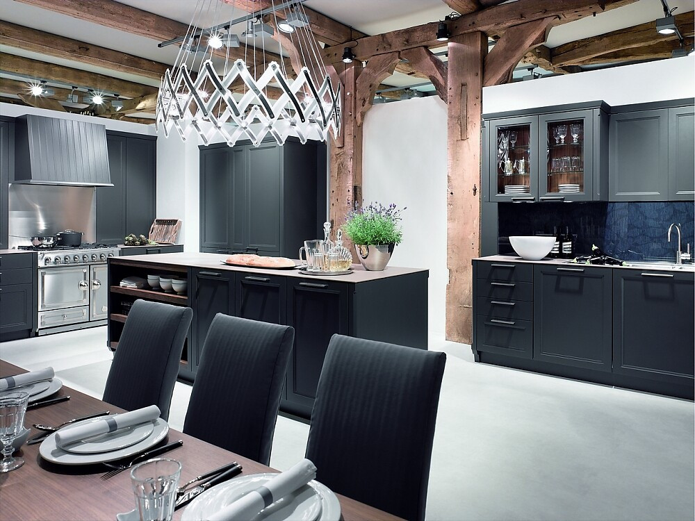 Deze open keuken heeft matzwarte kader fronten met grepen en een dun aanrechtblad. Passend is ook de bovenkast met glazen deurtjes. Hier uitgevoerd met een luxe fornuis. Zuordnung: Stil Landelijke keukens, Planungsart Open keuken (woonkeuken)