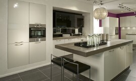 Eenkleurige eilandkeuken in moderne stijl met in de wand ingebouwde kasten. Het aanrechtblad komt over het kookeiland uit, waardoor zitgelegenheid ontstaat. Ook het werkbereik is in een soort nis ingebouwd. Zuordnung: Stil Moderne keukens, Planungsart Keuken met keukeneiland