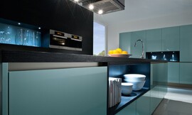 Deze pure design keuken valt op door de massieve marineblauwe hoogglans fronten die geheel greeploos zijn. Het donkerbruine aanrechtblad met subtiel reliëf in het hout geeft deze keuken een volwassen uiterlijk. Boven het kookeiland hangt een passende design afzuigkap. Zuordnung: Stil Design-keukens, Planungsart Keuken met keukeneiland