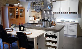 Moderne keuken met kookeiland en open rek voor kookgerei daarboven. Het kookeiland heeft een zithoek met stoelen op normale hoogte aangevoegd en een ingebouwd wijnrek. Zuordnung: Stil Moderne keukens, Planungsart L-vormige keuken