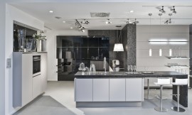 Greeploze keuken met stenen aanrechtblad en zitgelegenheid aan bar. Strakke lichtgrijze fronten en hoogglans zwarte fronten. Kraan centraal op keukeneiland. Zuordnung: Stil Moderne keukens, Planungsart U-vormige keuken