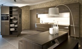 Deze moderne ééndelige keuken wordt afgemaakt door een vrijstaande kast waar zich twee apparaten in bevinden. De greeploze hoogglans fronten hebben net als het hout van de kast een bronzen tint. Zitgelegenheid aan aparte tafel. Zuordnung: Stil Moderne keukens, Planungsart Detail keukenontwerp