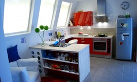 Twee onderkasten verbonden door een werkblad om aan te zitten. Hoogglans rode fronten en een design afzuigkap met glasplaat. De speelse retro look wordt afgemaakt met een vrijstaande koel-vriescombinatie. Zuordnung: Stil Moderne keukens, Planungsart Open keuken (woonkeuken)