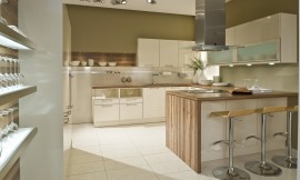 In deze U-vormige keuken is gebruik gemaakt van frisse witte fronten gecombineerd met een houten aanrechtblad dat aan de zijkant van het kookeiland doorloopt en ook als achtergrond bij een legplank is gebruikt. Aan de linkerkant zijn twee onderkasten opgenomen waarvan het bovenste gedeelte open is. Daarnaast komt de spoelkast en nog een onderkast. Boven de spoelbak zijn drie hangkastjes opgenomen. Links van de hangkastjes is een legplank bevestigd tegen hetzelfde hout als het aanrechtblad. Het andere wandgedeelte bestaat uit onderkasten, handige werkruimte op het aanrechtblad met daarboven twee brede kasten met glazen inzet en daaronder spotjes. Haaks hierop staat het kookeiland met fornuis, afzuigkap en aan de andere kant een gezellige zitgelegenheid. In de hoge wandkasten is de apparatuur opgenomen. Zuordnung: Stil Moderne keukens, Planungsart U-vormige keuken