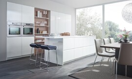 De stralend "firn"-witte hoogglans gelakte fronten hebben ergonomische greeplijsten in plaats van zichtbare grepen. Doordat het aanrechtblad van het keukeneiland uitsteekt ontstaat zitgelegenheid op barkrukken. De kastenwand is in de muur verzonken. Zuordnung: Stil Design-keukens, Planungsart Keuken met keukeneiland