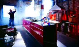 Greeploze design eilandkeuken met design afzuigkap en houten bar. Een glazen plaat verbindt het keukeneiland met de afzuigkap. De houten bar biedt verhoogde zitgelegenheid. Een zeer bijzonder kleurenspel. Zuordnung: Stil Luxe keukens, Planungsart Keuken met keukeneiland