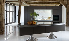 Vrij in de ruimte maar toch in zichzelf gesloten: met deze keuken wordt zichtbaar hoe design en functionaliteit in harmonie kunnen treden. Twee ronde metallic poten dragen dit matzwarte meubel. Een keukenwand met interessant verlichtingsconcept maakt het geheel af. Zuordnung: Stil Design-keukens, Planungsart Keuken met zitgelegenheid