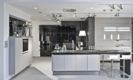 Greeploze keuken met stenen aanrechtblad en zitgelegenheid aan bar. Strakke lichtgrijze fronten en hoogglans zwarte fronten. Kraan centraal op keukeneiland. Zuordnung: Stil Moderne keukens, Planungsart U-vormige keuken