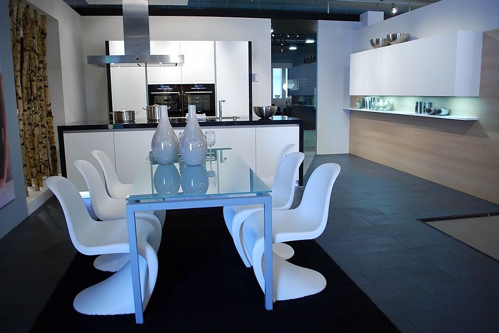 Zwart-witte keuken met greeploze fronten en blauwe verlichting in de sokkel. Hier ziet u de bijbehorende eettafel met glazen tafelblad en design stoelen. Zuordnung: Stil Design-keukens, Planungsart Open keuken (woonkeuken)