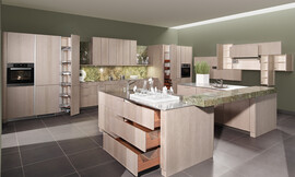 Moderne behaaglijkheid en absolute elegantie. Het oppervlakte is gebeitst in de tint &quot;zilver eik&quot;, waardoor deze topkeuken herinnert aan de natuurlijkheid van oude versleten houtplanken. Het binnenwerk van de lades in massief notenhout biedt een aangenaam, warm contrast met de koelere tint van de buitenkant van de meubels. Zuordnung: Stil Moderne keukens, Planungsart Keuken met keukeneiland